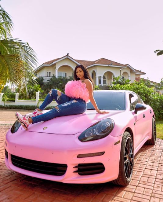 Hajia 4Real posing by her Porche Coupe 
