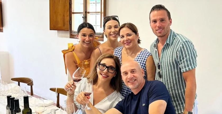 Linda Yaccarino and her husband toasting a glass of wine surrounded by their family in casual outfits.