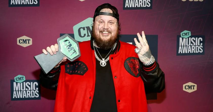 Jelly Roll smiles and poses on the CMT red carpet with a CMT award.